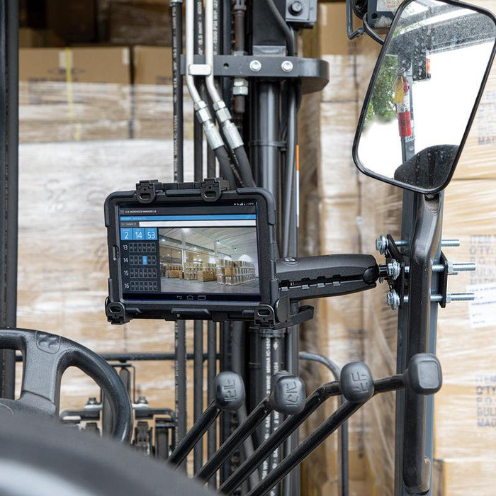 A LockVise™ Locking Forklift Front Guard Tablet Mount with a 10.25 inch Metal Robust™ Shaft is installed near the forklift’s controls and mirror, showing inventory software in a warehouse with stacked pallets and boxes.