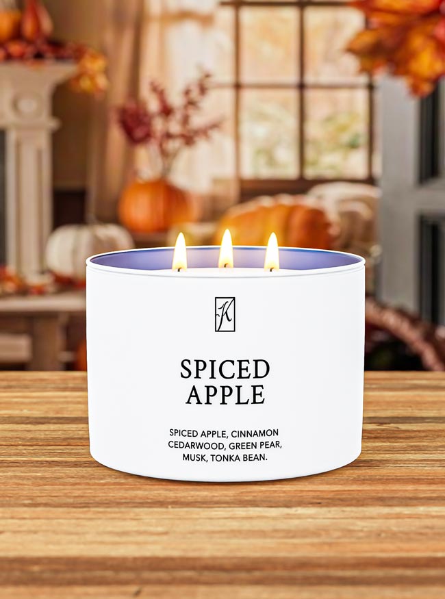Spiced Apple candle on a wooden surface with pumpkins and autumn decorations in the background.