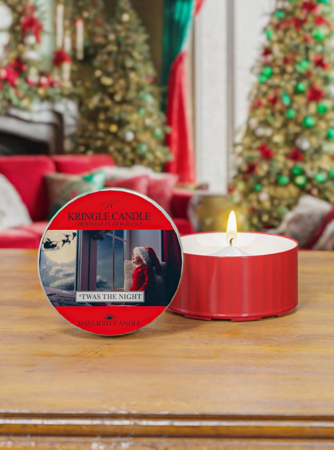Red Kringle Candle on a wooden surface with Christmas trees and decorations in the background