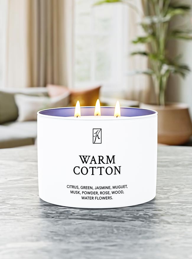 Candle labeled 'Warm Cotton' with a logo on a marble surface.