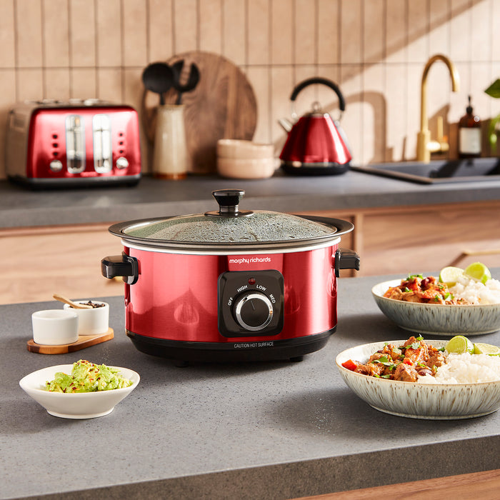 Red slow cooker on a kitchen counter with food and kitchen appliances in the background