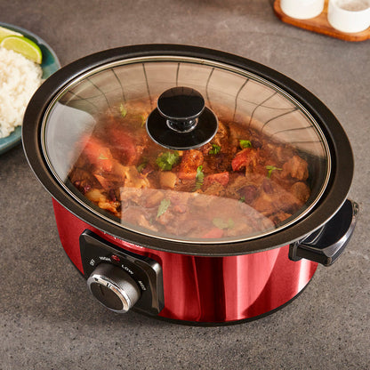 Red slow cooker with food inside on a grey surface