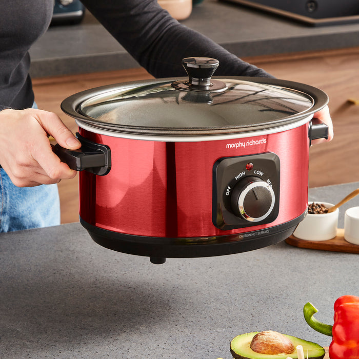 Red Morphy Richards slow cooker on a kitchen counter with a person holding it.