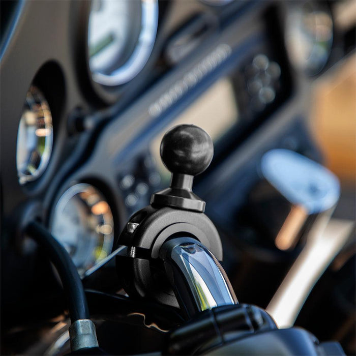 Close-up of a motorcycle handlebar featuring the Aluminum Motorcycle Handlebar Mount - 25mm (1 inch) Compatible, with dashboard instruments and gauges blurred in the background.