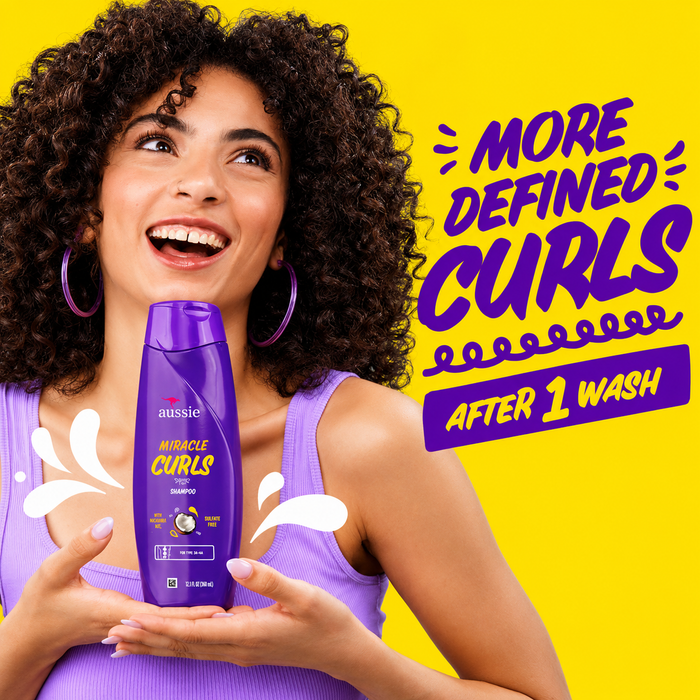 a promotional image featuring a smiling woman with defined curly hair holding aussie miracle curls shampoo in a purple bottle against a bright yellow background. bold text reads "more defined curls after 1 wash", highlighting curl definition and gentle cleansing with playful splash graphics.
