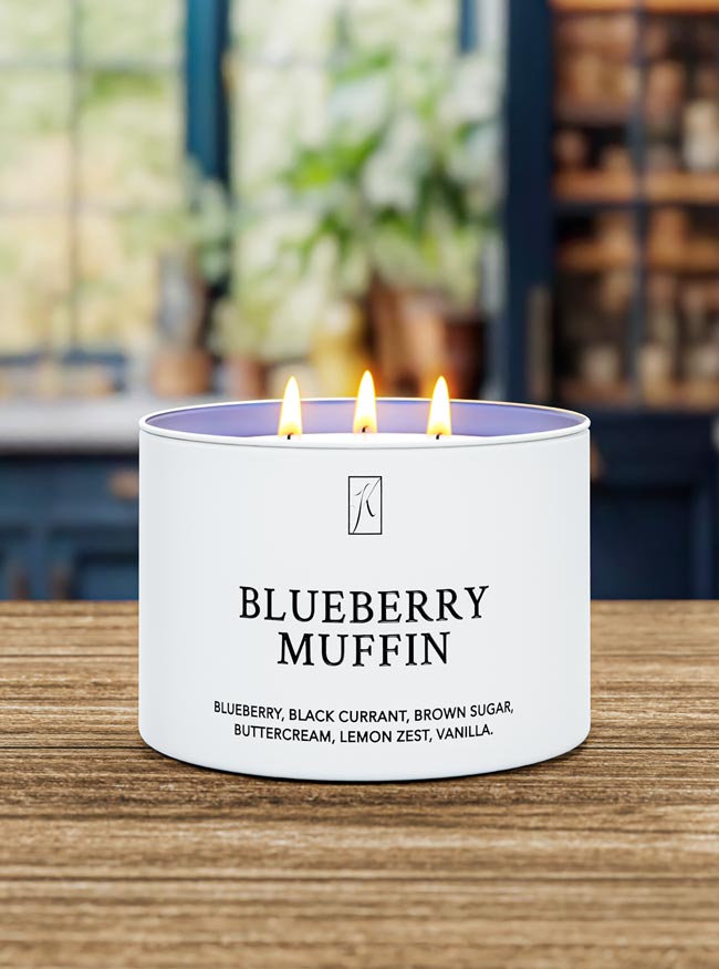 Candle labeled 'Blueberry Muffin' on a wooden surface with a blurred background