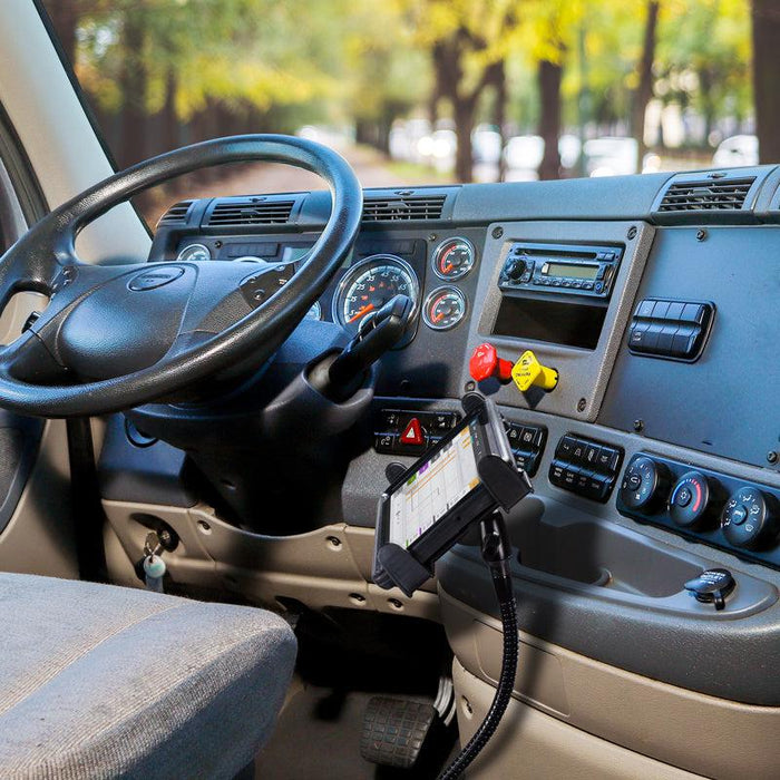 The interior of a truck cab displays the steering wheel, dashboard, and a Car or Truck Seat Rail Universal Slim-Grip® Tablet Mount with 28 inch Gooseneck by the seat rail, with trees visible through the windshield.