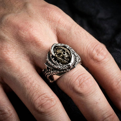 Silver claw devil ring with brass skull and crossbones centerpiece worn on man's finger, featuring detailed textured band with gothic biker style design against dark fabric background