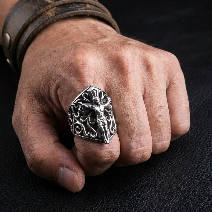 Sterling silver crucifix shield ring worn on man's index finger with leather bracelet