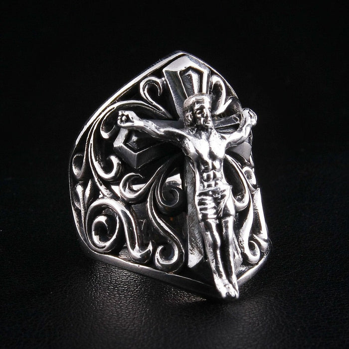 Angled view showing raised crucifix figure and intricate scroll design on silver ring