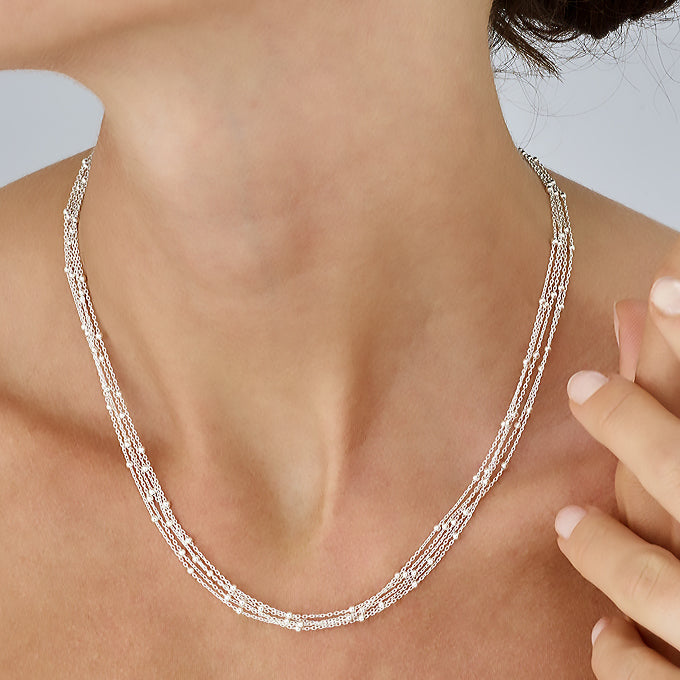 Kvinna som bär ett kort halsband i silver med tunna kedjor och små silverkulor.