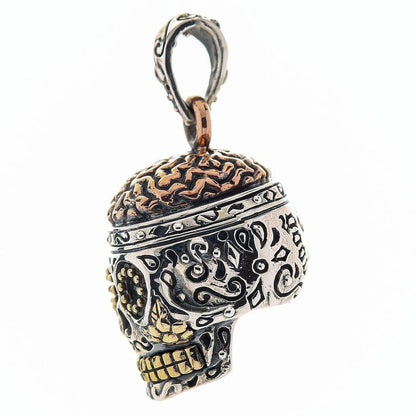 A detailed side view of a Día de los Muertos pendant, showing the fine craftsmanship of the copper brain and silver engravings.