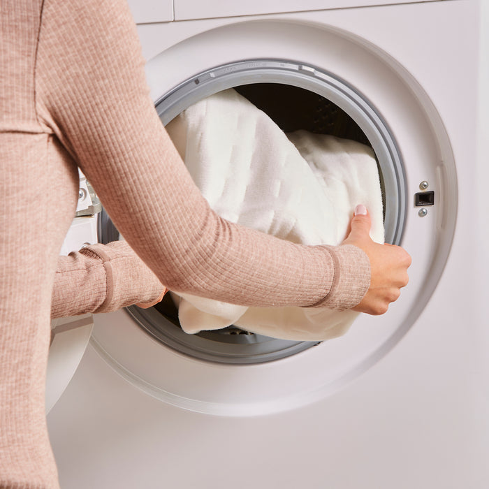 Person loading a white pillow into a washing machine