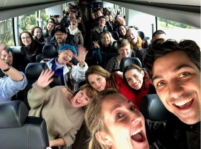 A group of people on a bus, raising their hands and interacting with the tour guide, likely during a break or at a stop on the bus tour.