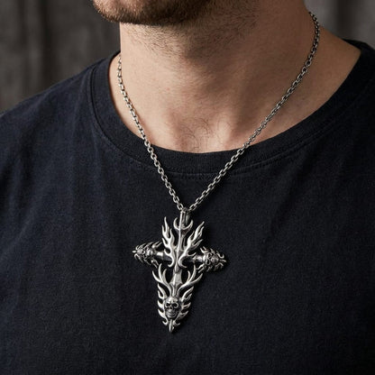 Close-up of a male model wearing a black t-shirt and a sterling silver gothic biker pendant necklace featuring a flame cross design with detailed skulls, hanging on a silver chain.