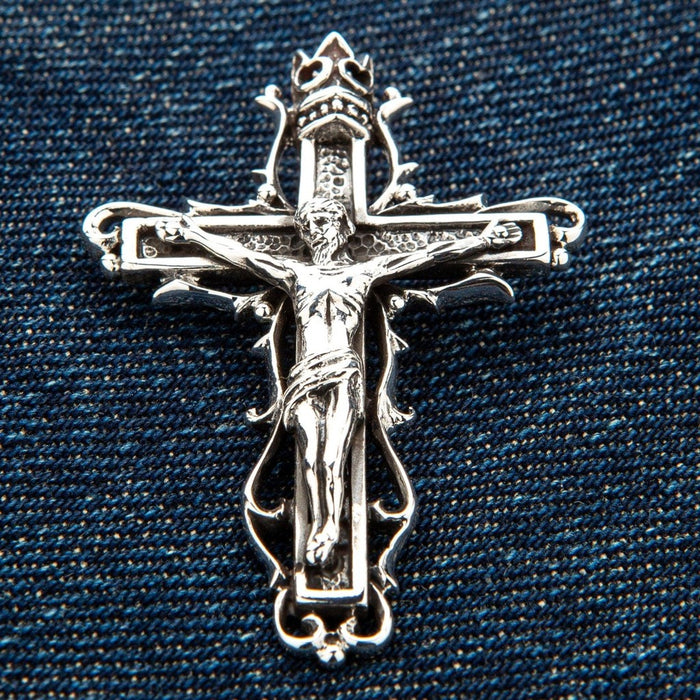 Gothic sterling silver crucifix pendant with crown and thorns displayed on blue denim fabric background