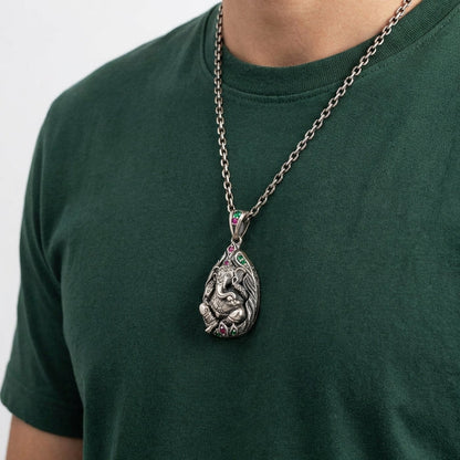 Hindu Ganesh sterling silver pendant with green and pink gemstone accents on a silver chain necklace worn by a man in a dark green t-shirt
