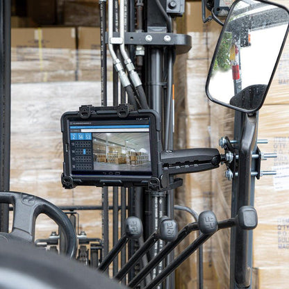 A LockVise™ Locking Forklift Front Guard Tablet Mount with a 10.25 inch Metal Robust™ Shaft is installed near the forklift’s controls and mirror, showing inventory software in a warehouse with stacked pallets and boxes.