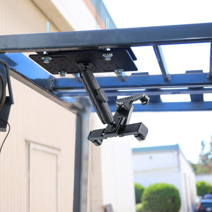 The LockVise™ Locking Forklift Overhead Guard Tablet Mount with 6 metal shaft is attached beneath a blue metal rack outdoors, with adjustable arms—perfect for securely holding tablets or electronic devices.
