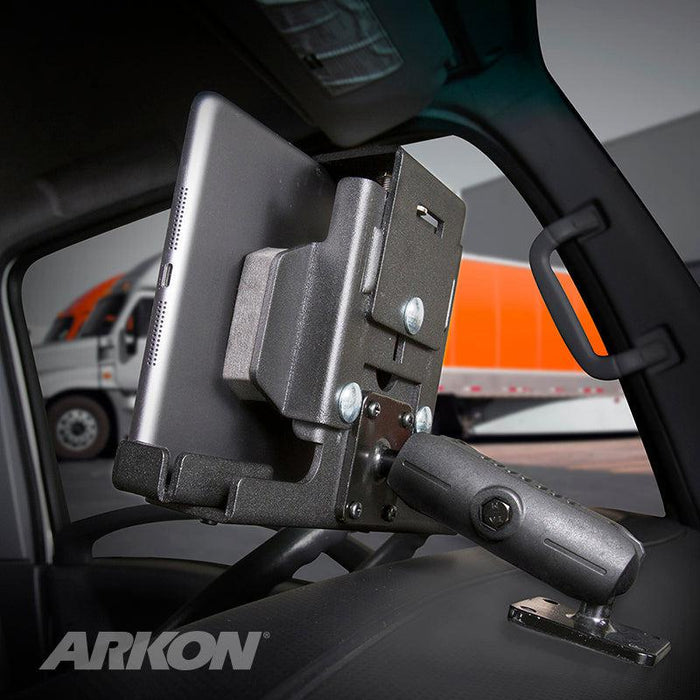 A LockVise™ Metal Locking Tablet Mount with Drill Base and Magnetic Micro USB Charge Cable for Commercial and Enterprise secures a tablet to a vehicle’s dashboard, with a semi-truck outside. The ARKON logo appears in the bottom left corner.