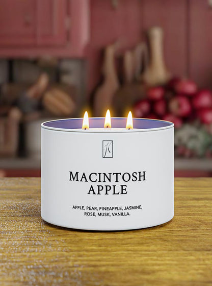 Candle labeled 'Macintosh Apple' with flames on a wooden surface, blurred kitchen background