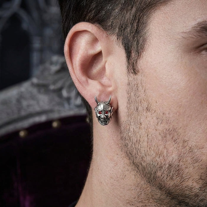Close-up of a male model wearing a gothic silver Oni mask stud earring featuring red gemstone eyes.