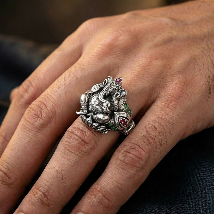 Close-up of a detailed sterling silver Lord Ganesha ring set with small red and green gemstones worn on a man's ring finger.