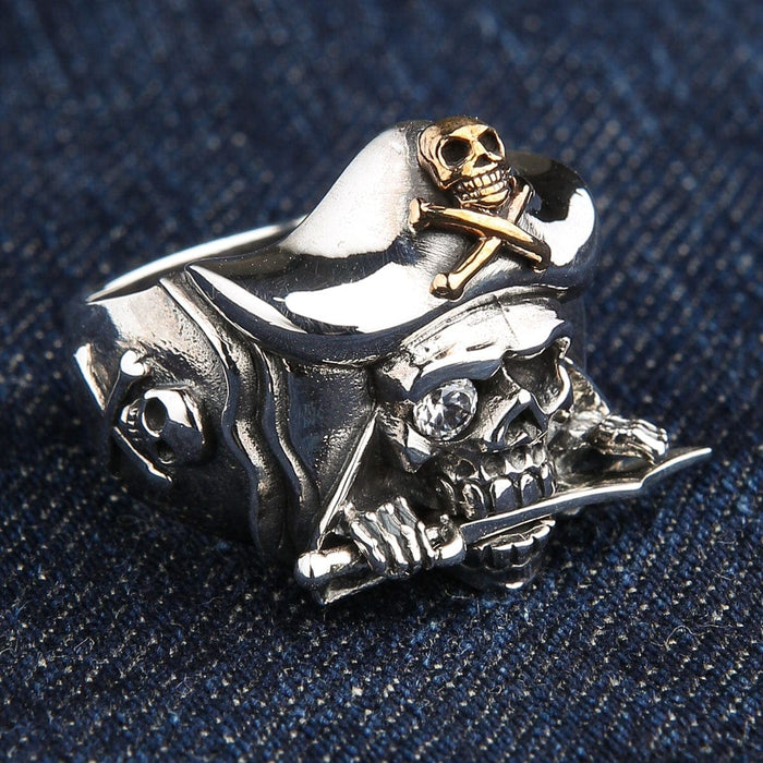A solid sterling silver pirate skull ring with a 14k gold-plated Jolly Roger on its hat, a dagger in its teeth, and a sparkling gem eye.