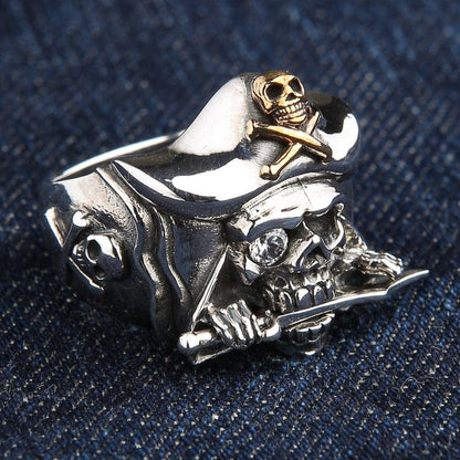 A solid sterling silver pirate skull ring with a 14k gold-plated Jolly Roger on its hat, a dagger in its teeth, and a sparkling gem eye.