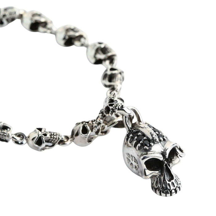 A solid sterling silver punk skull bracelet with a chain of detailed skulls and a larger, black-jeweled skull charm.