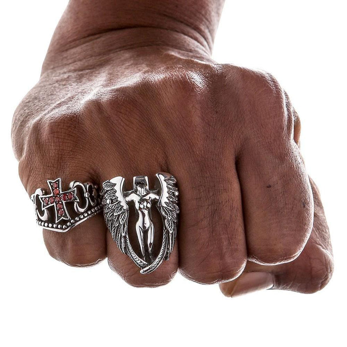 Clenched fist displaying the red CZ cross ring worn alongside a large winged silver statement piece.