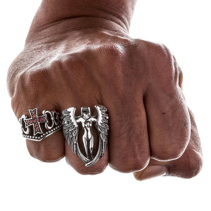 Clenched fist displaying the red CZ cross ring worn alongside a large winged silver statement piece.