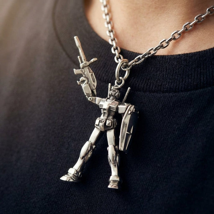 A detailed silver RX78-2 Gundam pendant necklace worn by a person in a black t-shirt, showing the robot holding a gun and shield.