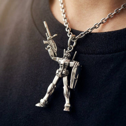 A detailed silver RX78-2 Gundam pendant necklace worn by a person in a black t-shirt, showing the robot holding a gun and shield.