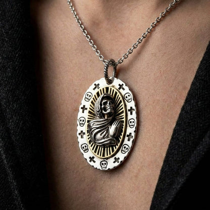 Santa Muerte silver pendant necklace featuring a robed skeleton figure with radiating halo design, surrounded by skulls and crosses on white enamel border, worn on silver chain against skin with black clothing