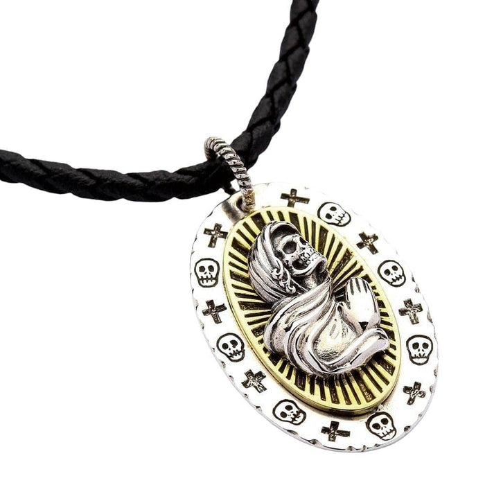 A two-tone Santa Muerte pendant necklace, showing the silver praying skeleton against a brass halo, worn on a leather cord.
