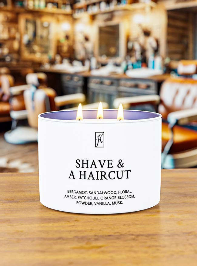 Candle labeled 'Shave & A Haircut' on a wooden surface with a barbershop background