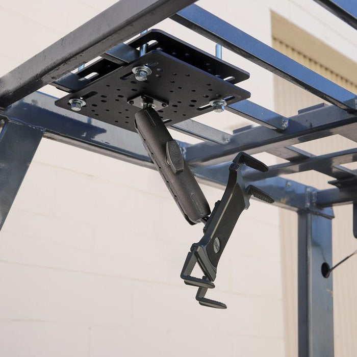 A Slim-Grip® Tablet Holder with Forklift Overhead Guard Mount and 6 Metal Shaft securely installed under a metal frame outdoors by a beige brick wall.