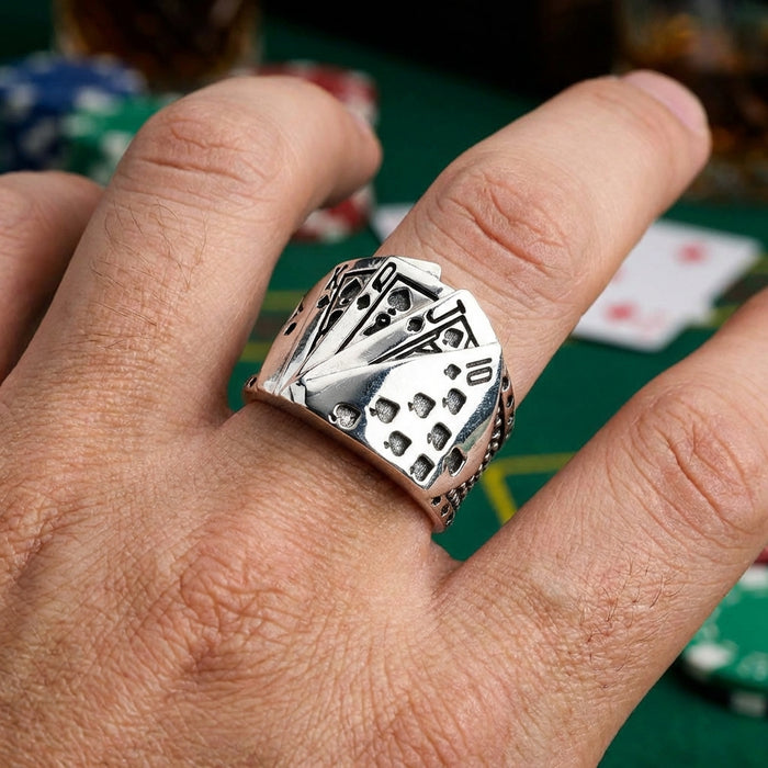 Sterling silver Royal Flush of Spades poker ring featuring engraved playing cards design worn on a man's finger with casino poker chips and cards in the background