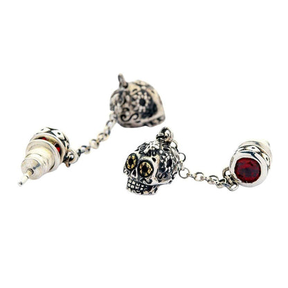 A close-up detail shot of a two-part skull earring, clearly showing the red stone stud and the dangling sugar skull charm.