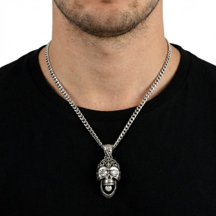 Close-up of a male model wearing a silver tribal skull pendant necklace featuring diamond-studded eyes and mouth, styled over a black t-shirt.