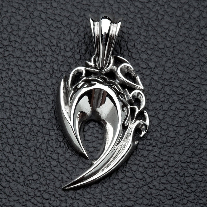 A front view of the sterling silver tribal fang pendant with flame engravings, resting on a black leather surface.