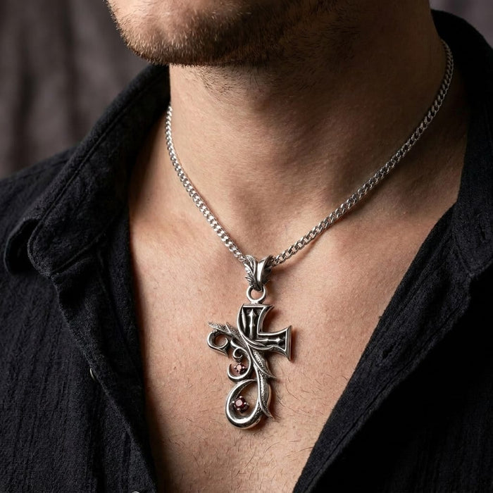 Close-up of a male model wearing an ornate silver tribal gothic cross pendant featuring two small red stones on a silver chain, styled with an open black button-down shirt.