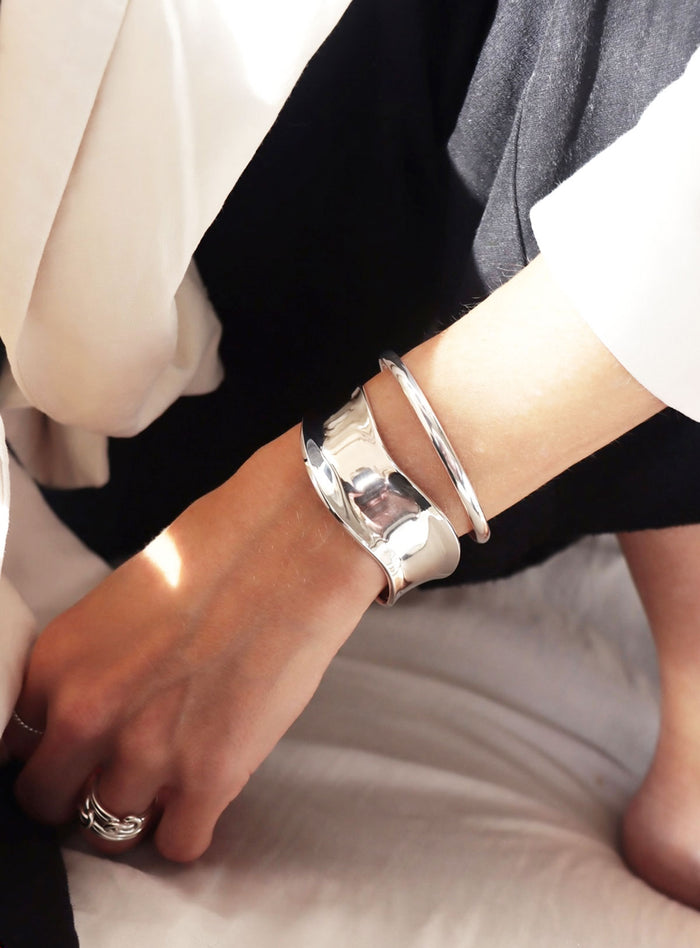 Kvinna som bär ett brett cuff armband i blankt silver och silverringar.