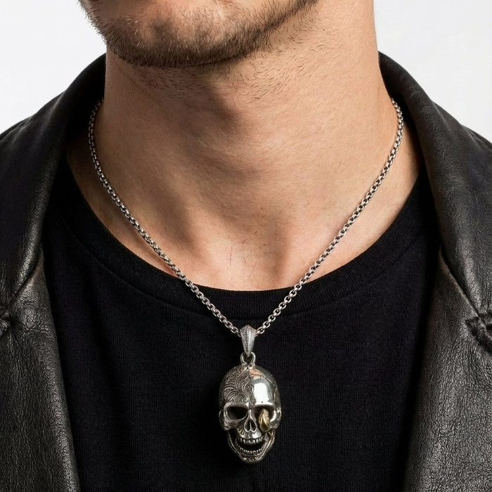 Man wearing a detailed silver skull pendant necklace with intricate engraved patterns on the cranium and gold accent tooth, styled with a black t-shirt and leather jacket